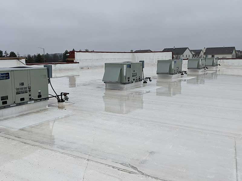 Row of AC units on a flat, white commercial roof after a downpour