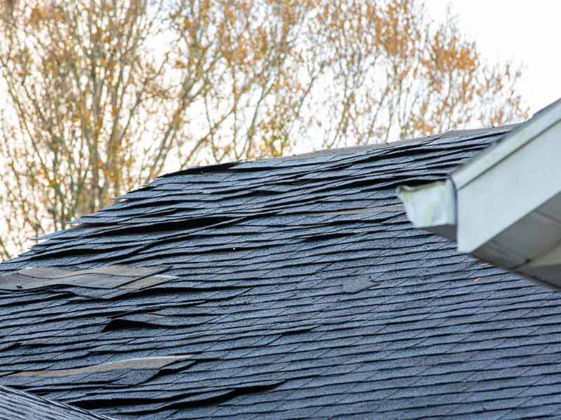 Close up of damaged and loose gray shingles on a residential roof caused by a storm