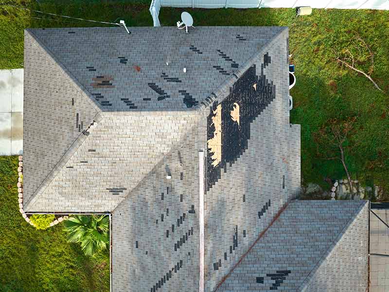 Top view of a Florida home with damaged and missing gray shingles due to Hurricane Ian
